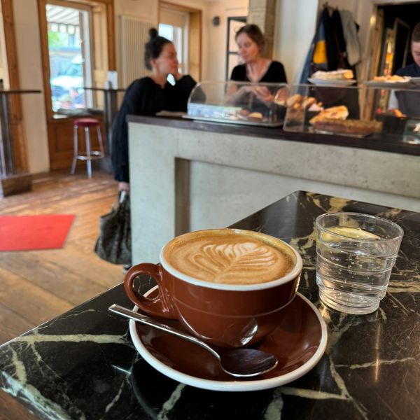 Cappuccino im Café Moulu in Stuttgart auf Marmortisch, gemütliches Café mit Barista und Kuchentheke im Hintergrund - ideal für ein Kaffee-Date
