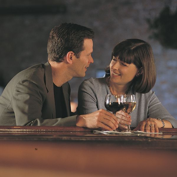 Zwei Singles stoßen lächelnd mit Wein in einer gemütlichen Bar an. Es zeigt wie wichtig Bars für Dates in Dresden sind.