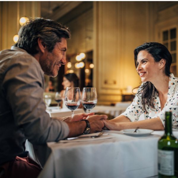 Ein Paar sitzt sich lächelnd bei einem romantischen Dinner mit Wein gegenüber. Ein stilvolles Ambiente, das typische Restaurants für Dates in Dresden perfekt widerspiegelt.