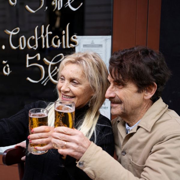 Zwei fröhliche Singles stoßen mit Bier vor einer Bar an. So wichtig sind Bars für Dates in Dresden.