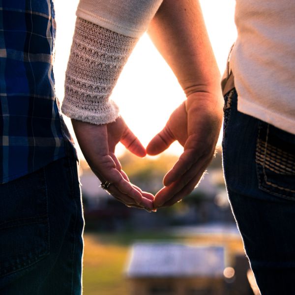 Zwei Menschen formen mit ihren Händen ein Herz im Sonnenlicht. Es zeigt Dankbarkeit beim Dating, Nähe und Vertrauen.