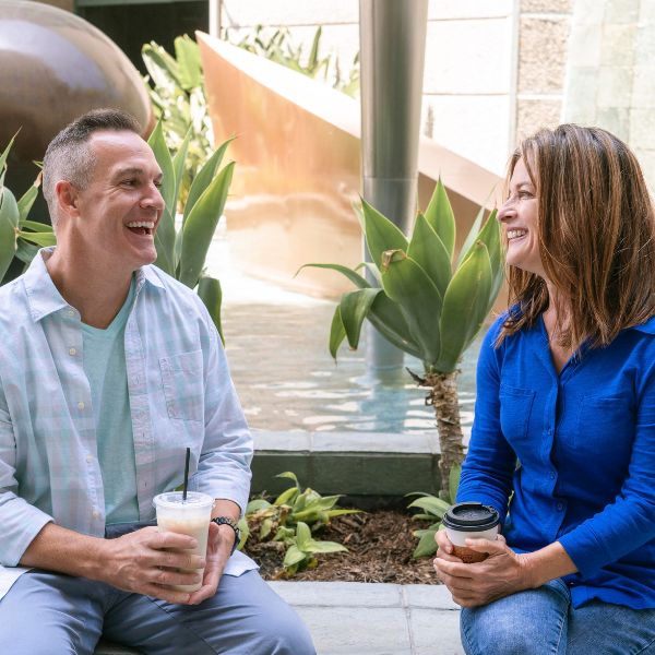 Mann und Frau mittleren Alters sitzen lachend bei einem Kaffee zusammen. Es zeigt die Leichtigkeit und Dankbarkeit beim Dating.