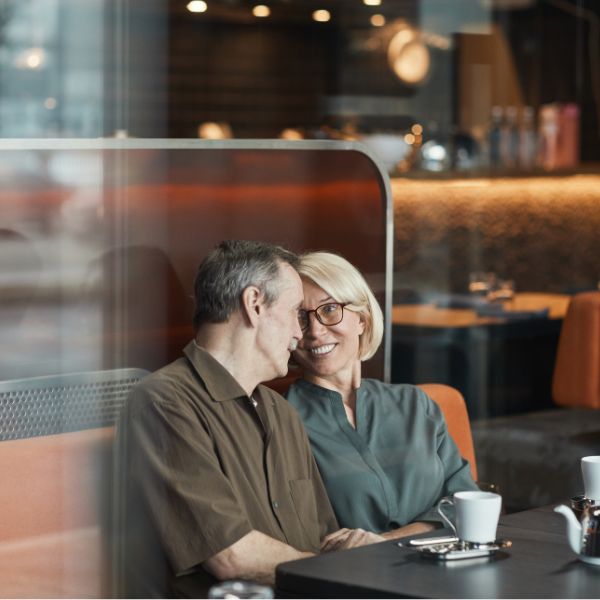 Ein lächelndes Paar über 40 sitzt in einem gemütlichen Kölner Café, schaut sich liebevoll an und genießt die gemeinsame Zeit bei Kaffee und Gesprächen. Es beweist, dass Dating über 40 auch noch schön sein kann.