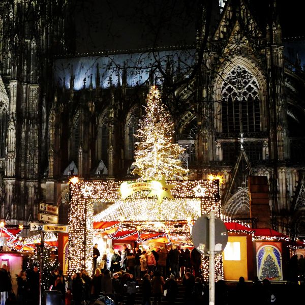 Festlich beleuchteter Weihnachtsmarkt am Kölner Dom mit Lichterketten, Weihnachtsbaum und Besuchern. Eine stimmungsvolle Szene, die den Zauber deutscher Weihnachtsmärkte für Singles zeigt.